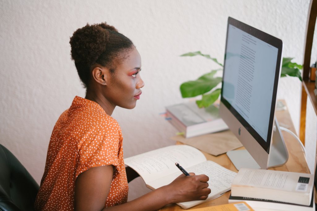 Person sitting at a desk, taking notes while reading information on a computer screen