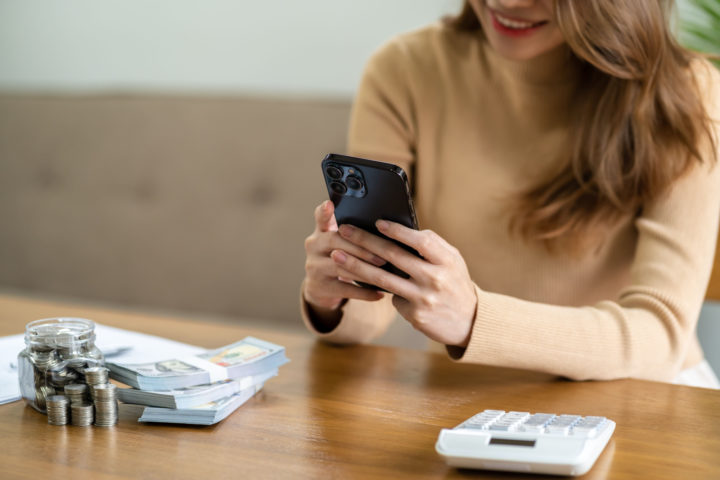 Woman holds phone at table next to pile of money and calculator