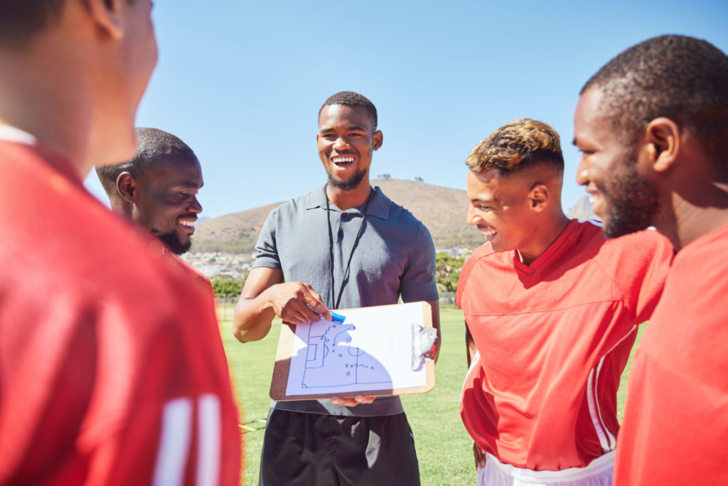 Sports coach discussing tactics with a group of players on a sports field
