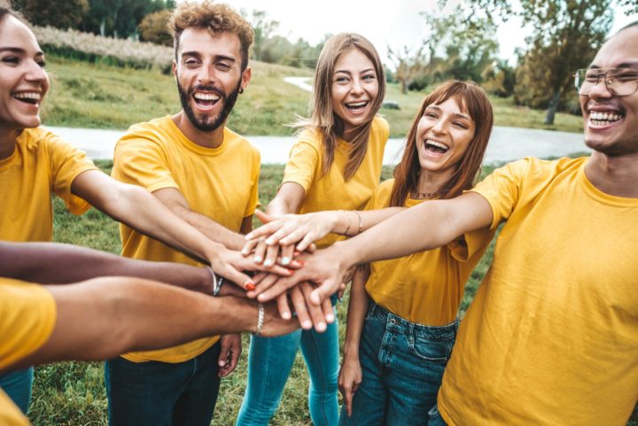 Group of smiling people stand in circle joining hands in centre