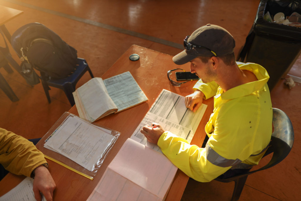 Man in high vis sits at table filling in forms