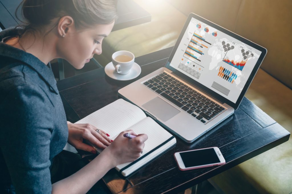 A woman sits making notes in front of a laptop
