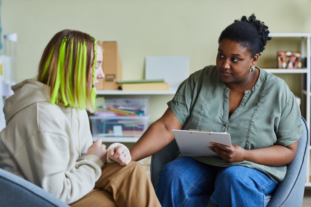 Two people having a supportive one-to-one conversation, one holding a clipboard and listening attentively
