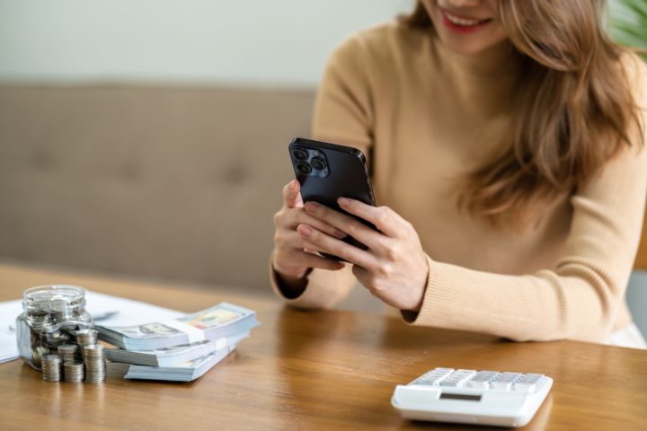 Woman holds smartphone with money and a calculator on a table