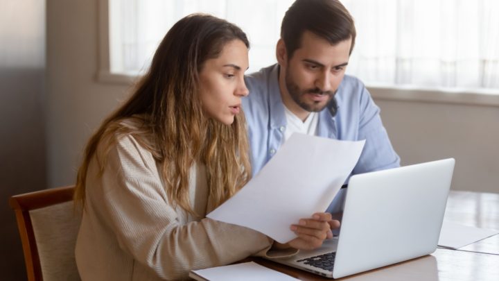 Two people sit at laptop, a woman holds a document