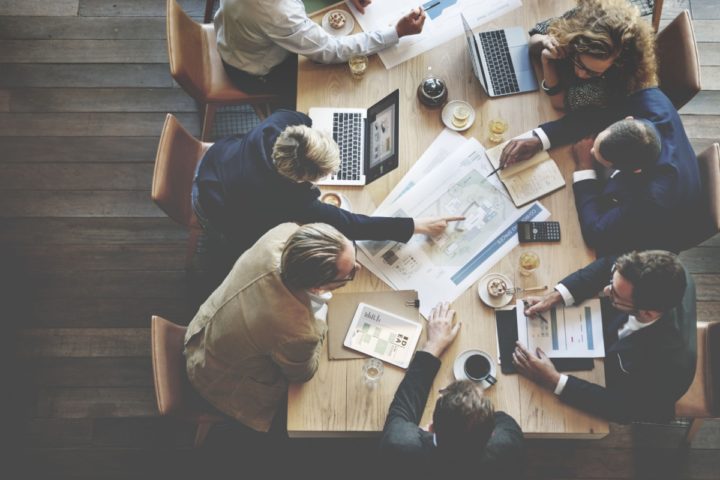 Aerial shot of people sat around a table looking at laptops and charts