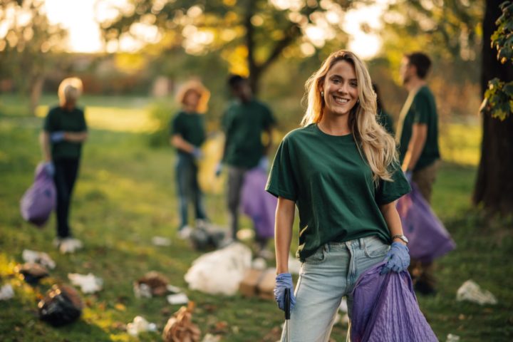 A woman stands in front of a group of people collecting litter in a park