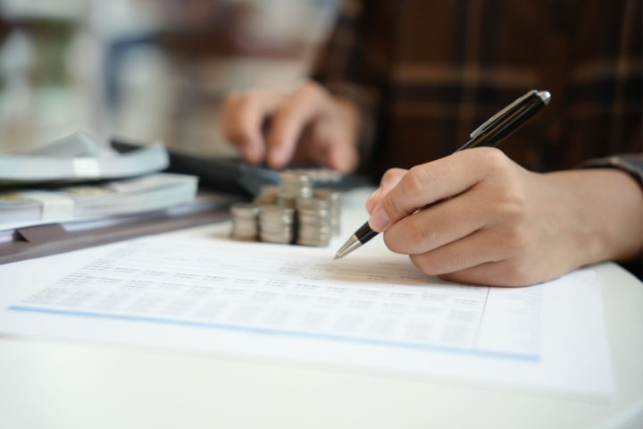 Person's hands holding a pen next to some money, using a calculator