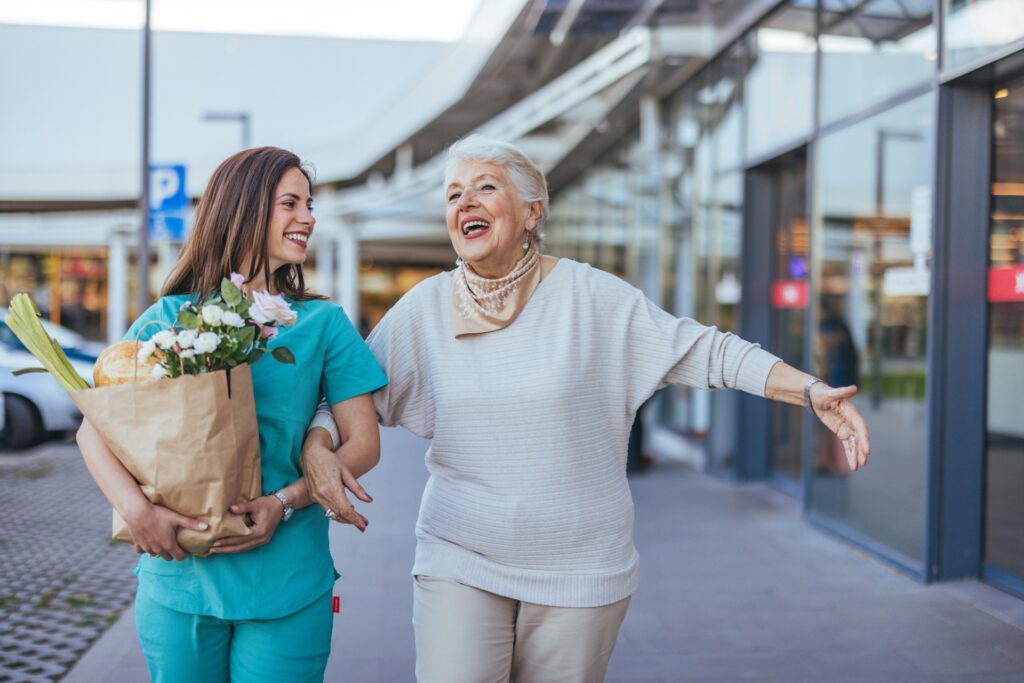 Care worker walking with an older woman carrying a bag of groceries and flowers