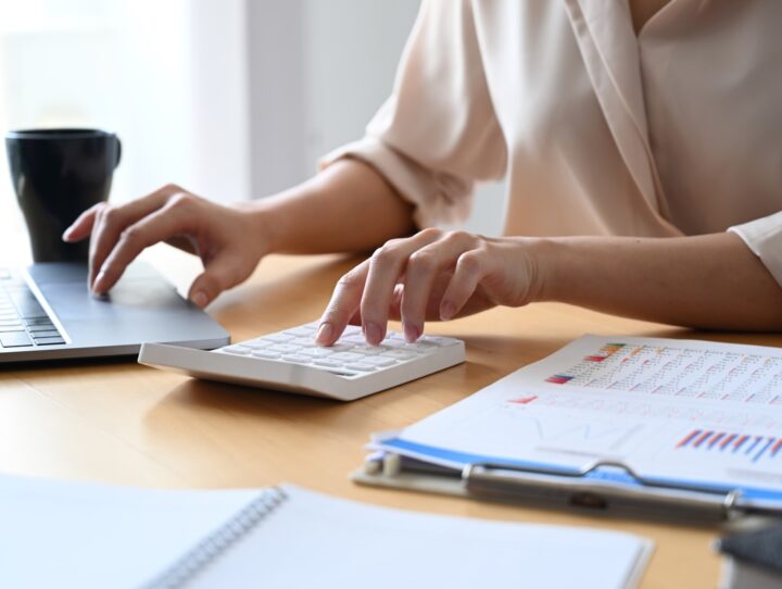 A woman's hands using a calculator and a laptop