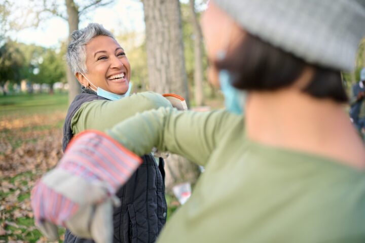 Smiling woman with a face mask greets another person by touching elbows