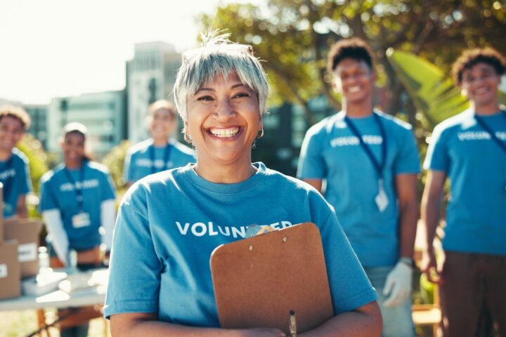 Smiling woman in a blue t-shirt holds a clipboard, other smiling volunteers stand behind her